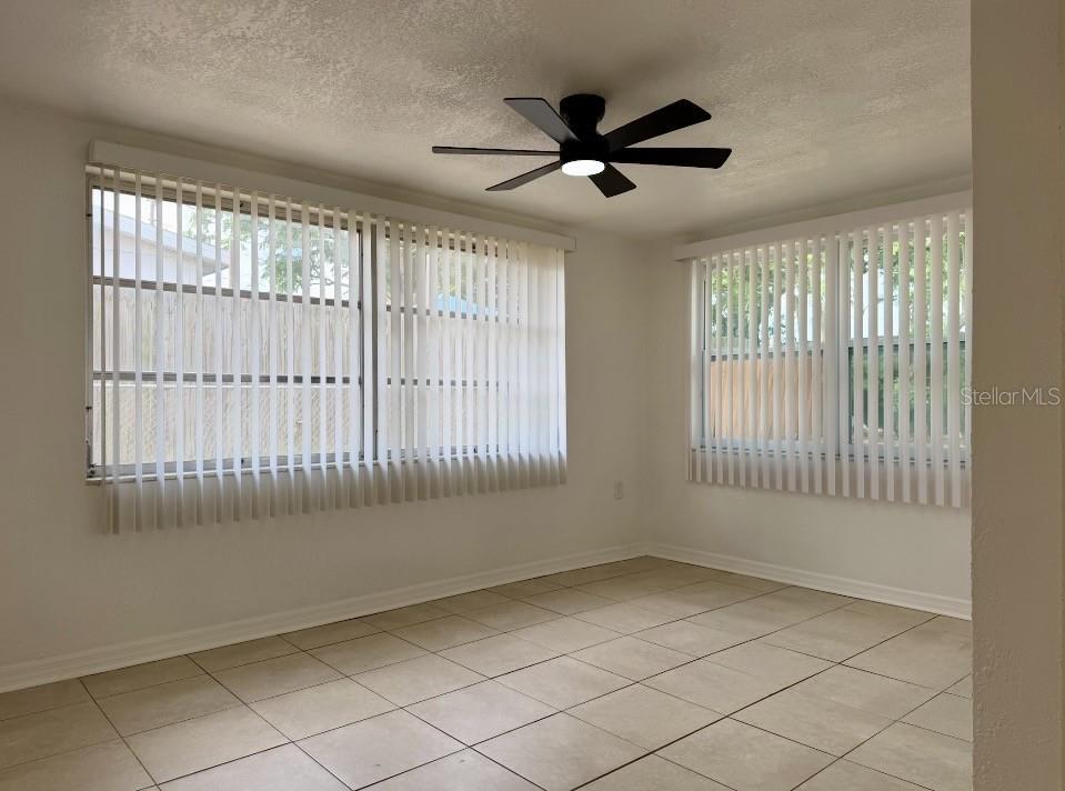 An empty room features light-colored tile flooring, white walls, vertical blinds, and a ceiling fan — 7412 UNIVERSITY DRIVE, HUDSON, FL