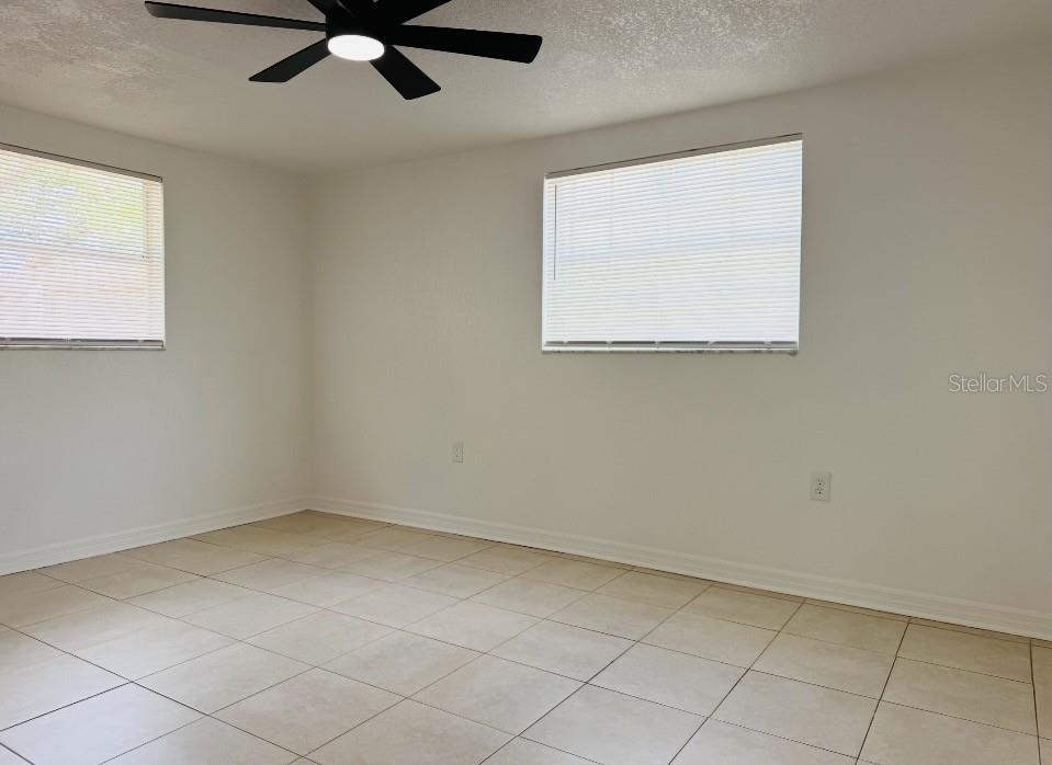 An empty bedroom features white walls, tile flooring, two windows with blinds, and a ceiling fan — 7412 UNIVERSITY DRIVE, HUDSON, FL