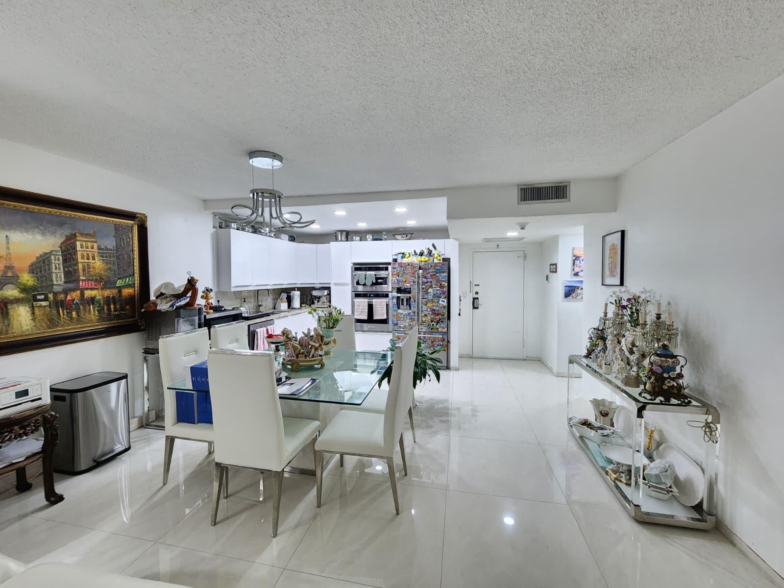 A dining area with a glass table and white chairs sits adjacent to a modern kitchen — 2500 Parkview Drive # 403, Hallandale Beach FL 33009, HALLANDALE BEACH, FL