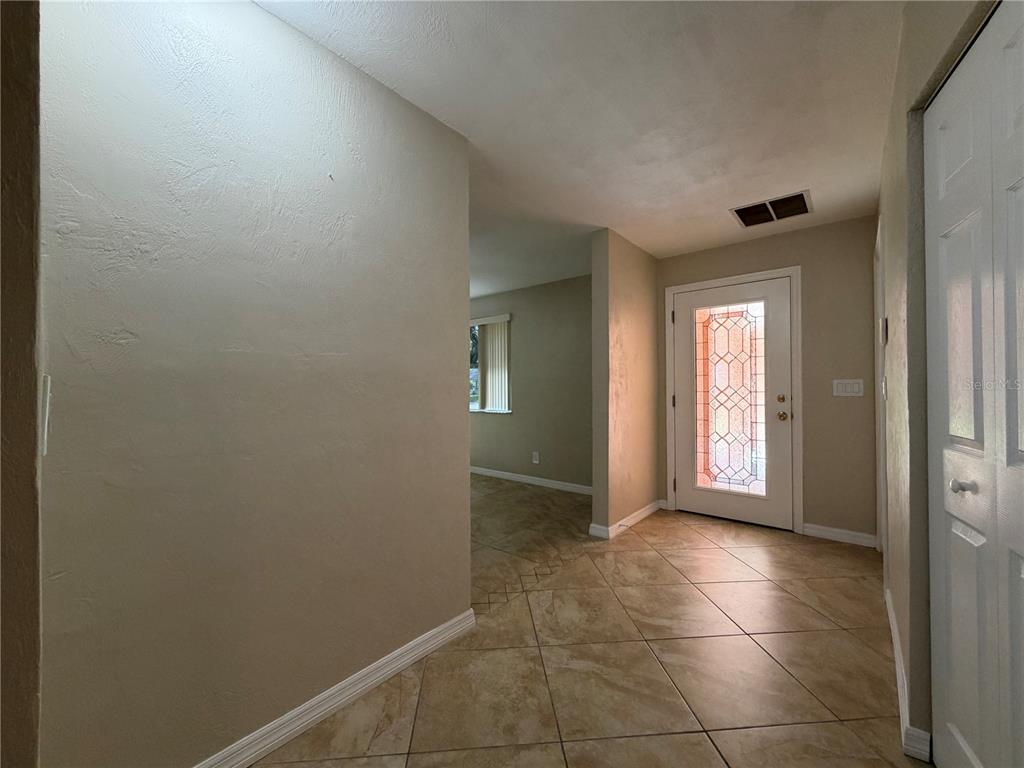 An entryway features tan tile flooring, a white front door with decorative glass, and beige walls — 1013 INDIAN OAKS E, HOLLY HILL, FL