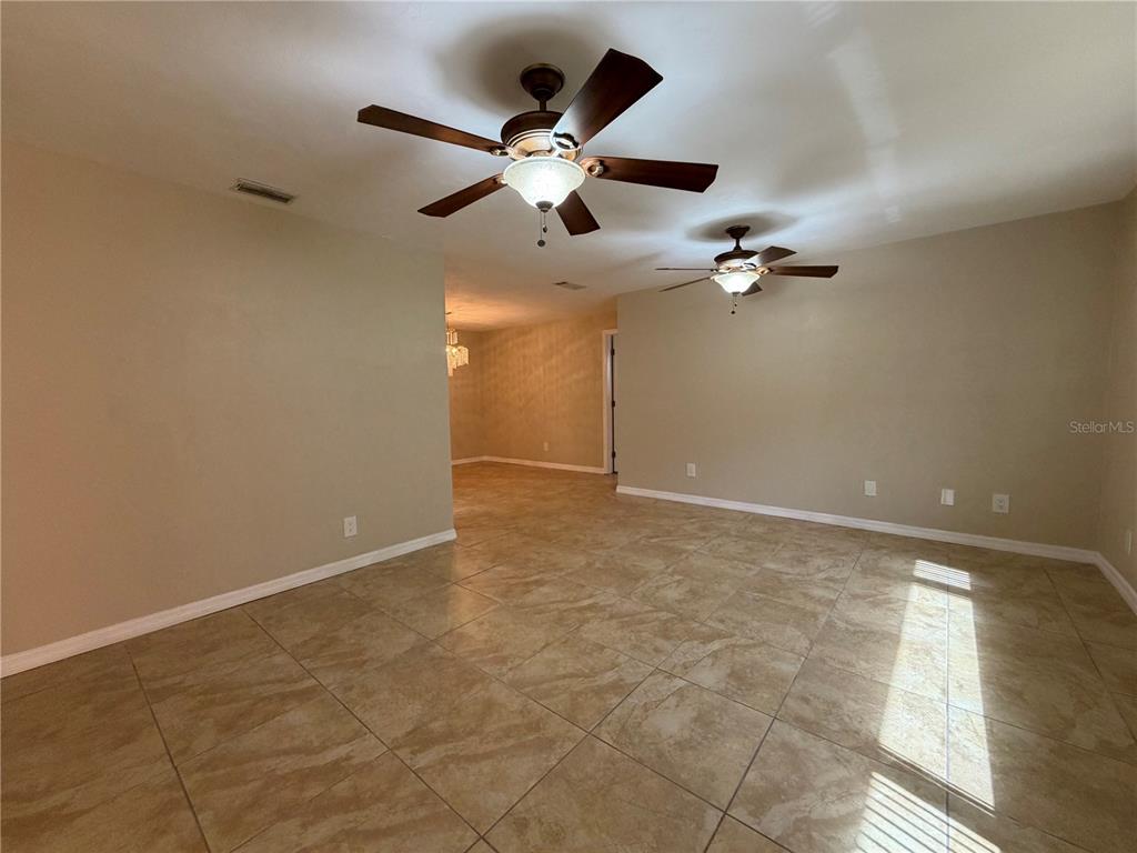 An open living area features beige tile flooring, two ceiling fans, and neutral wall paint — 1013 INDIAN OAKS E, HOLLY HILL, FL