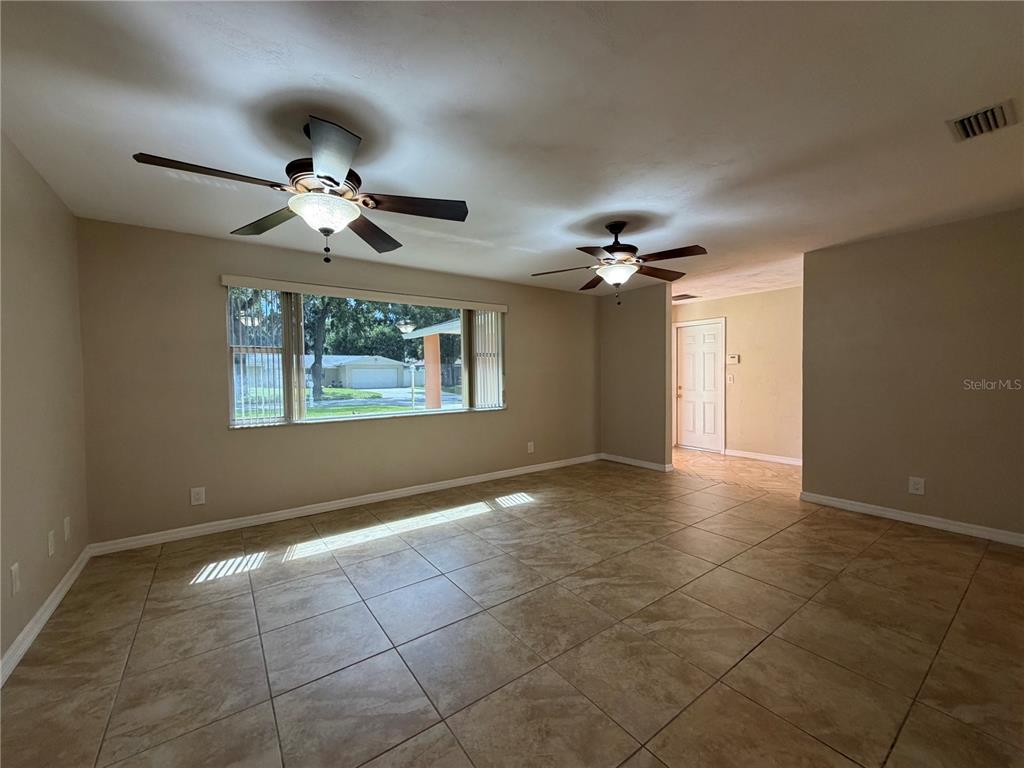 A living room features large beige floor tiles, two ceiling fans, and a wide window — 1013 INDIAN OAKS E, HOLLY HILL, FL