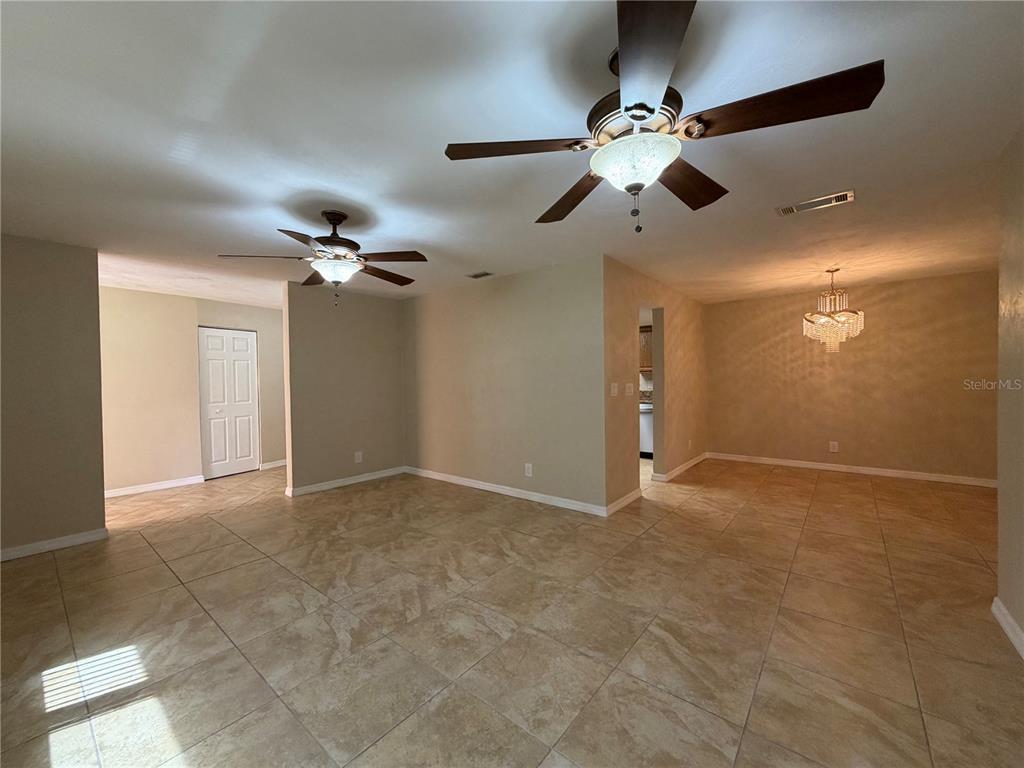 An open-concept living and dining area features beige tile flooring and two ceiling fans — 1013 INDIAN OAKS E, HOLLY HILL, FL