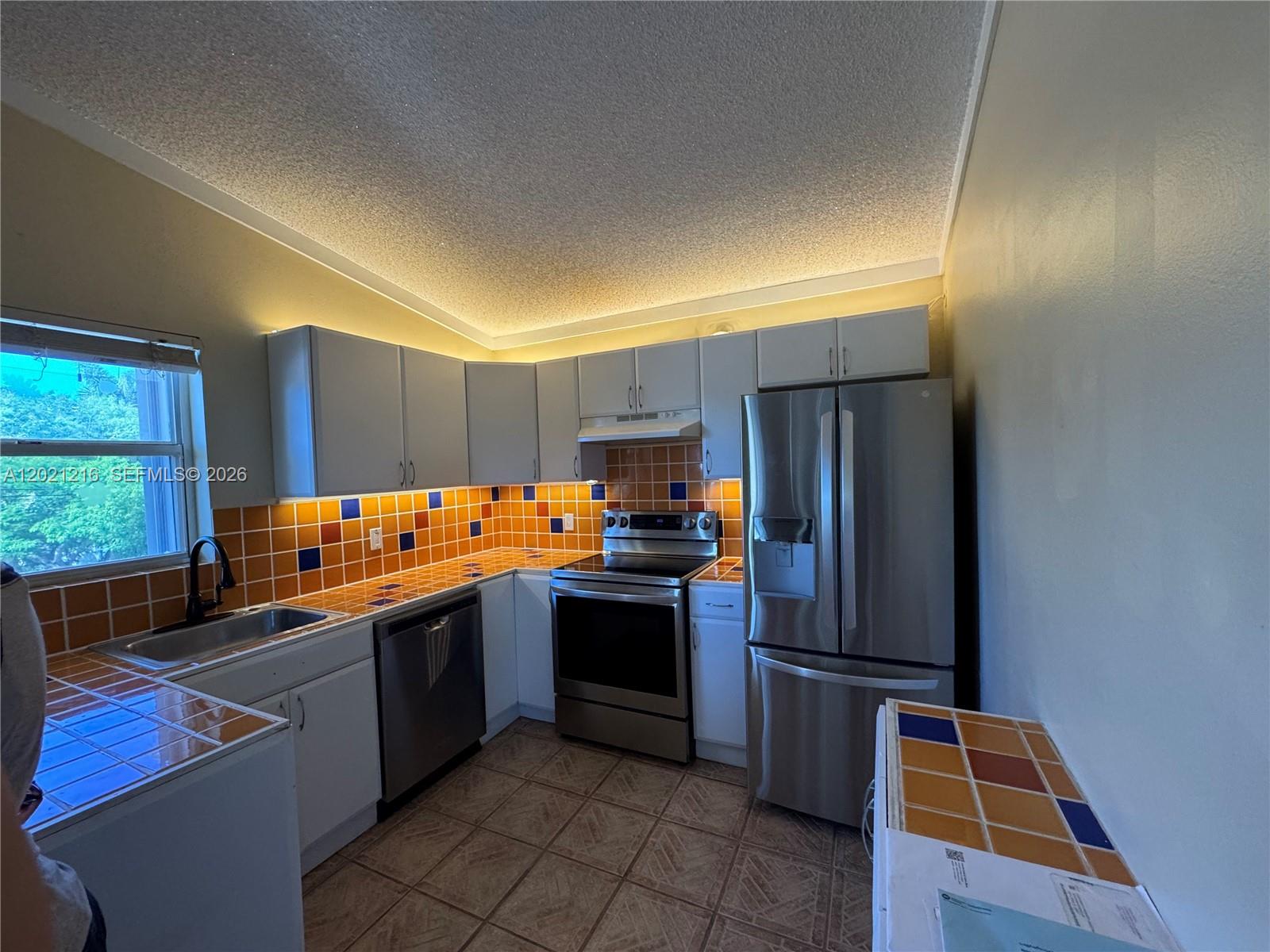 A kitchen features white cabinets, stainless steel appliances, and orange and blue tiled countertops — 104 Ocean Shores Drive, Key Largo FL 33037, KEY LARGO, FL