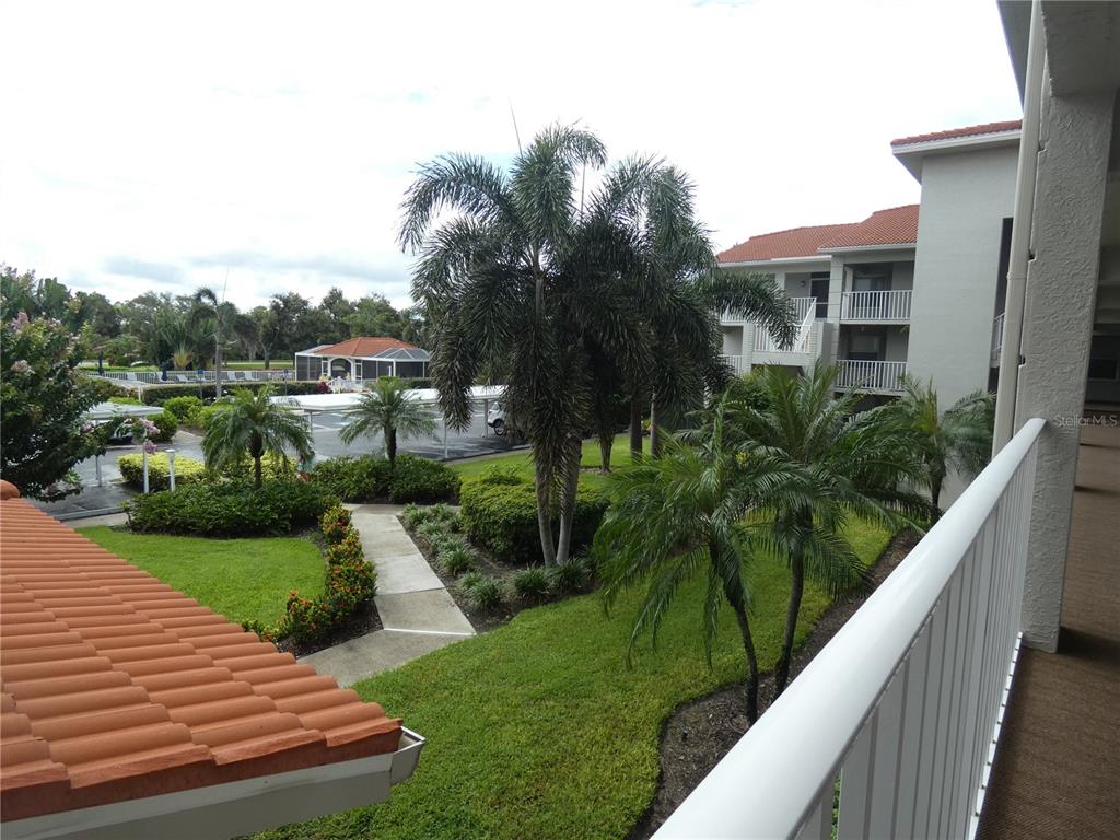 A view from a balcony overlooking a landscaped courtyard, palm trees, and a parking area — 9320 CLUBSIDE CIRCLE UNIT 2208, SARASOTA, FL