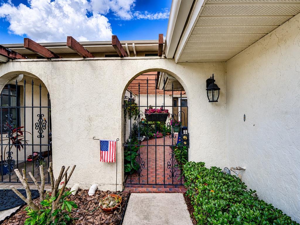 An exterior view shows a stucco wall with two arched iron gates and a brick walkway — 100 S TREMAIN STREET UNIT G2, MOUNT DORA, FL