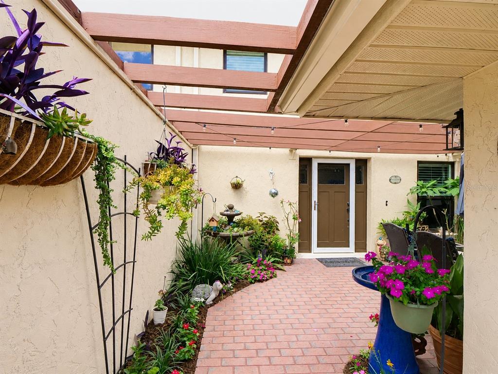 A brick-paved courtyard features a pergola, hanging plants, a small fountain, and a front door — 100 S TREMAIN STREET UNIT G2, MOUNT DORA, FL