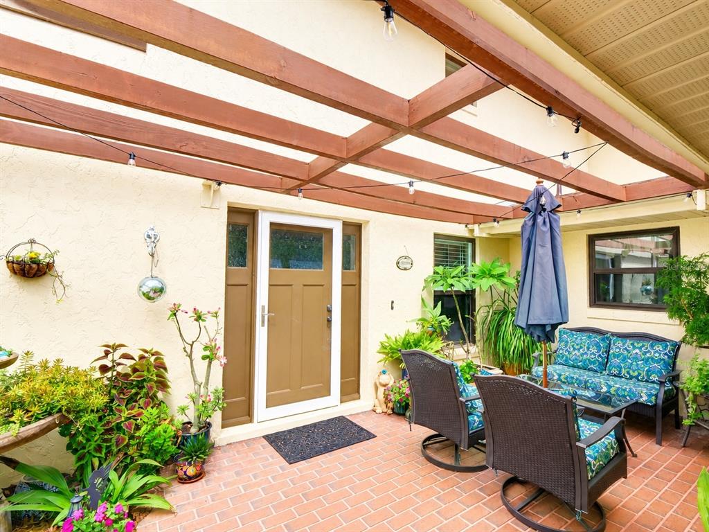 A brick patio features a wooden pergola, outdoor seating, and potted plants near a doorway — 100 S TREMAIN STREET UNIT G2, MOUNT DORA, FL