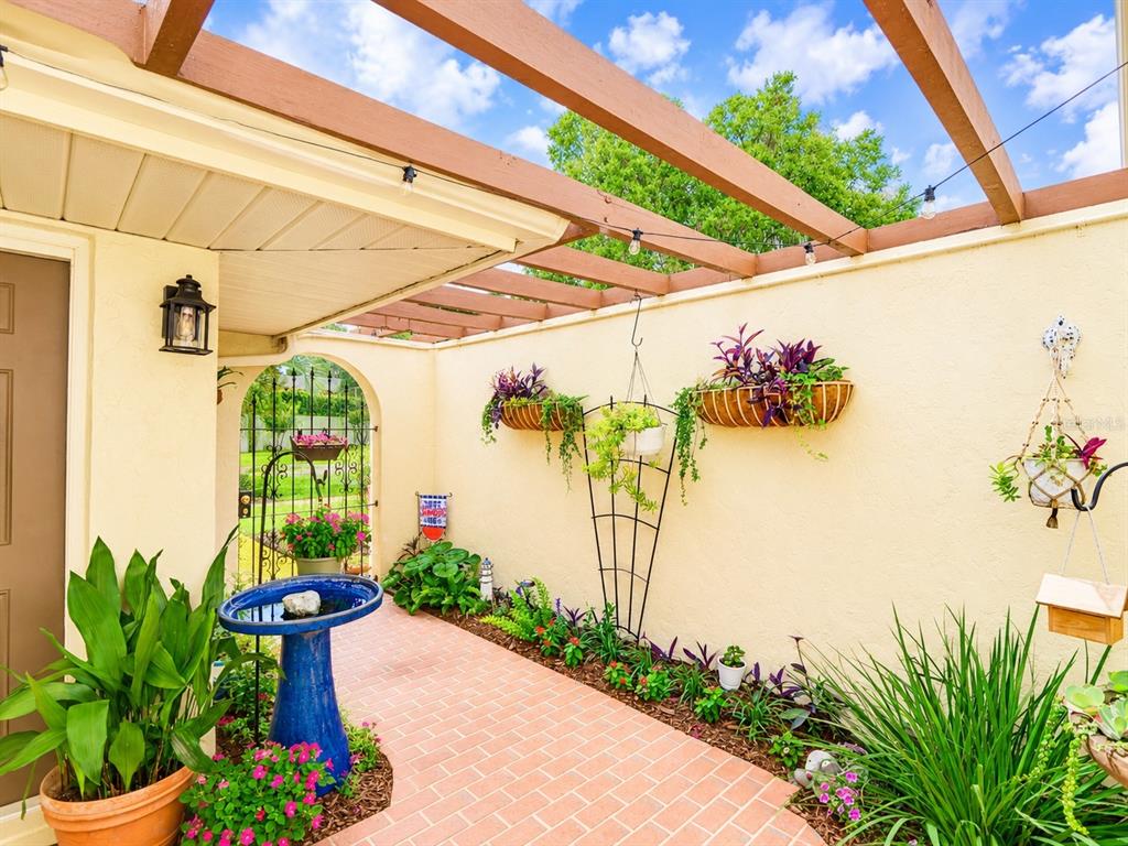 A brick patio features a blue birdbath, hanging planters, and a wooden pergola overhead — 100 S TREMAIN STREET UNIT G2, MOUNT DORA, FL