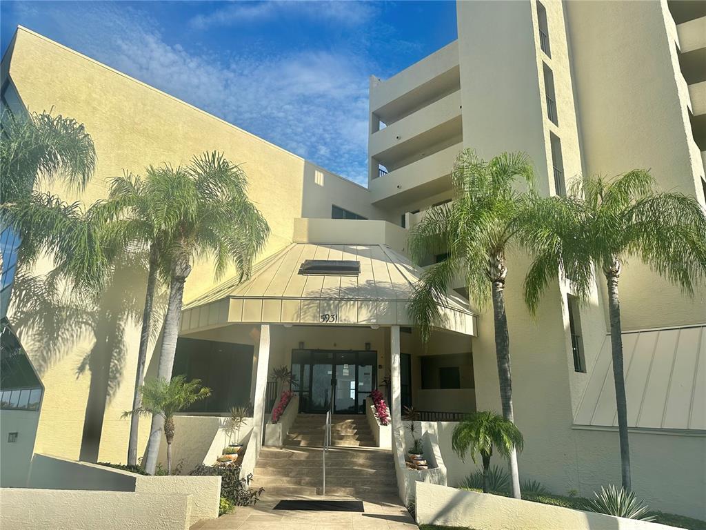 The exterior of a multi-story building features a covered entrance with stairs and palm trees — 6009 SEA RANCH DRIVE UNIT 704, HUDSON, FL