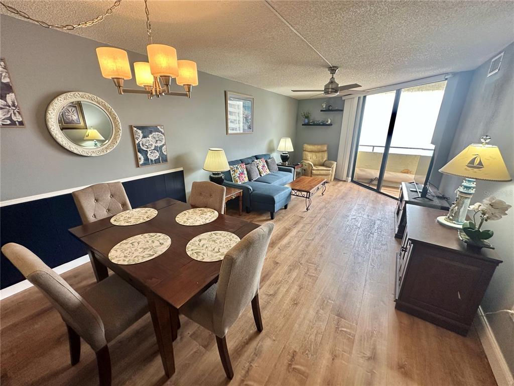 An open-concept living and dining area features wood-look flooring, a blue sofa, and balcony access — 6009 SEA RANCH DRIVE UNIT 704, HUDSON, FL