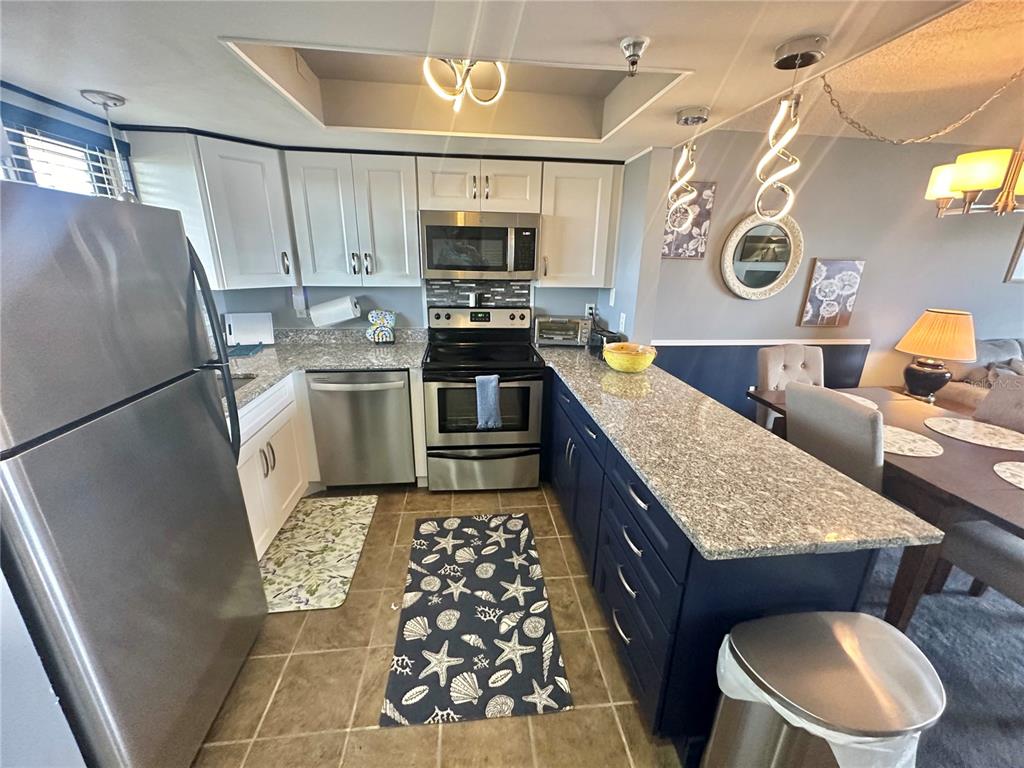 A kitchen features white upper cabinets, dark blue lower cabinets, granite countertops, and stainless appliances — 6009 SEA RANCH DRIVE UNIT 704, HUDSON, FL