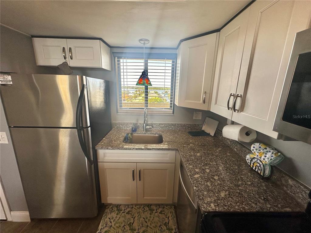 A kitchen features white cabinets, granite countertops, stainless steel appliances, and a window view — 6009 SEA RANCH DRIVE UNIT 704, HUDSON, FL