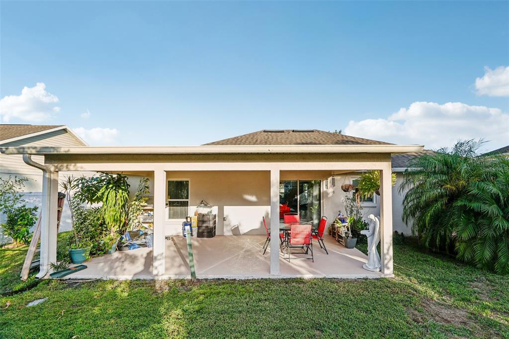 A covered concrete patio features a dining set, a statue, and surrounding landscaping — 4604 SOUTHPORT BAY DRIVE, KISSIMMEE, FL
