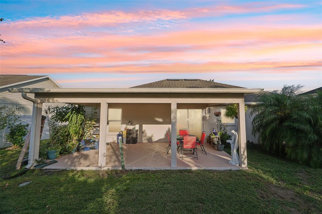 A covered concrete patio features a dining set and a statue in a grassy backyard — 4604 SOUTHPORT BAY DRIVE, KISSIMMEE, FL