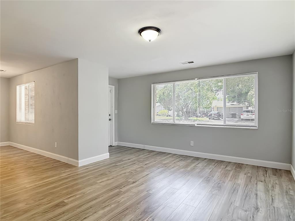 An empty room features light gray walls, wood-look flooring, a ceiling light, and large windows — 1495 GRANADA AVENUE, DAYTONA BEACH, FL