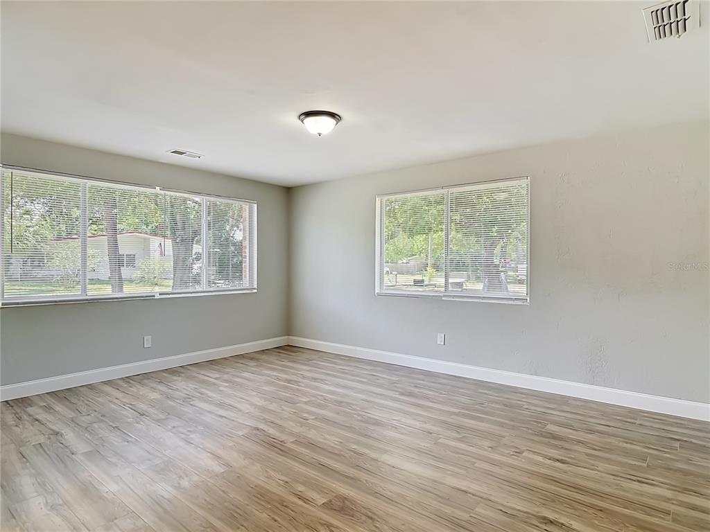 An empty room features light gray walls, wood-look flooring, and two windows with blinds — 1495 GRANADA AVENUE, DAYTONA BEACH, FL