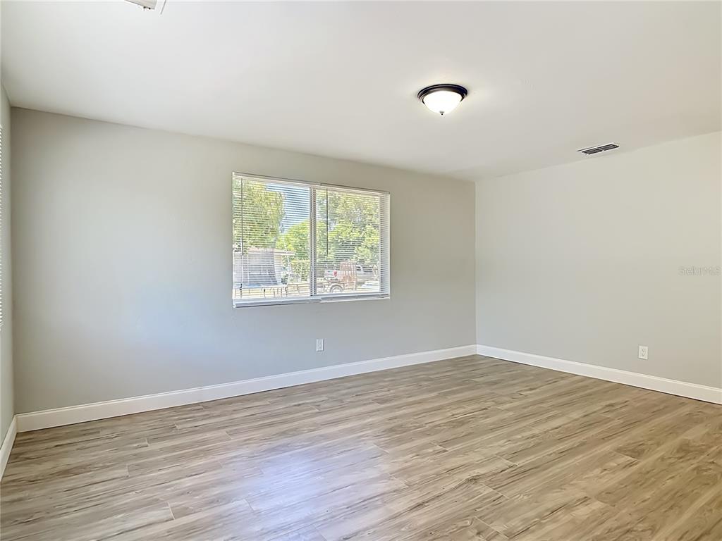 An empty room features light gray walls, wood-look flooring, a window with blinds, and lighting — 1495 GRANADA AVENUE, DAYTONA BEACH, FL