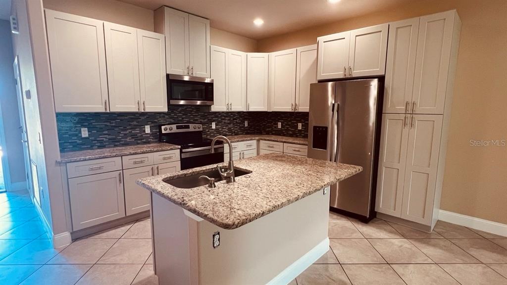 A kitchen features white cabinets, granite countertops, a central island, and stainless steel appliances — 57 COLUMBIA LANE UNIT B, PALM COAST, FL