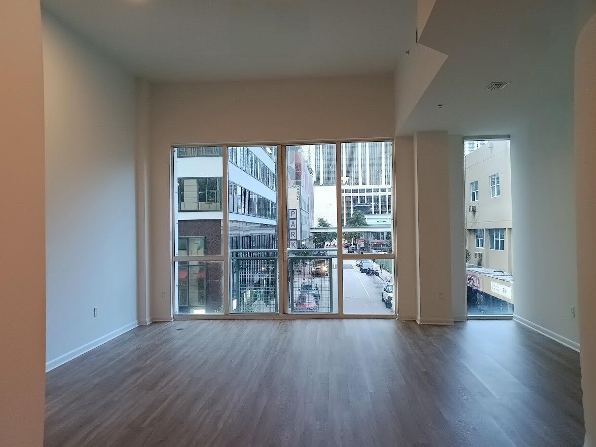 An empty room with wood-look flooring and large windows overlooking a city street — 253 NE 2nd Street # 221, Miami FL 33132, MIAMI, FL