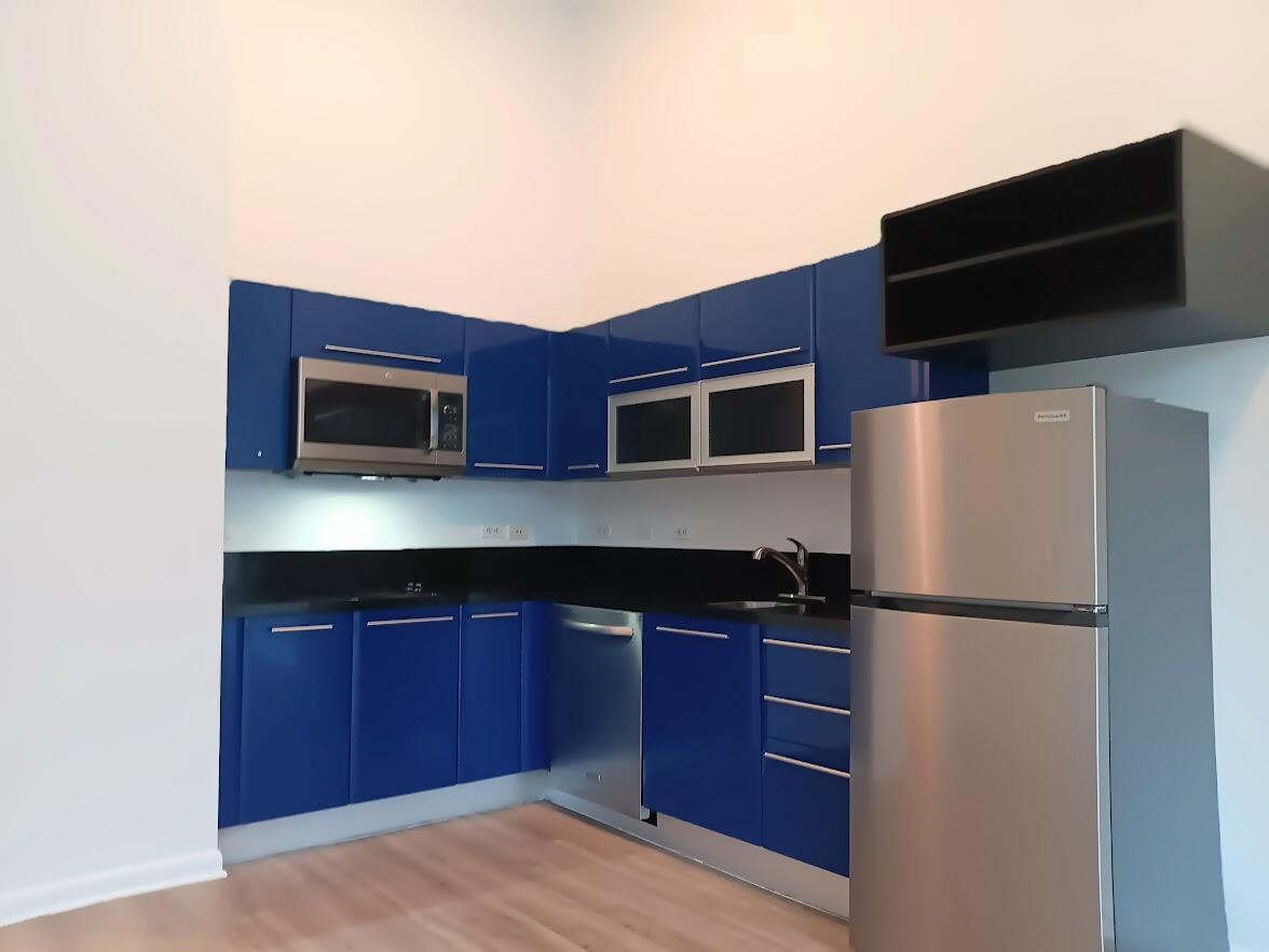 A kitchen features blue cabinets, black countertops, stainless steel appliances, and light wood flooring — 253 NE 2nd Street # 221, Miami FL 33132, MIAMI, FL