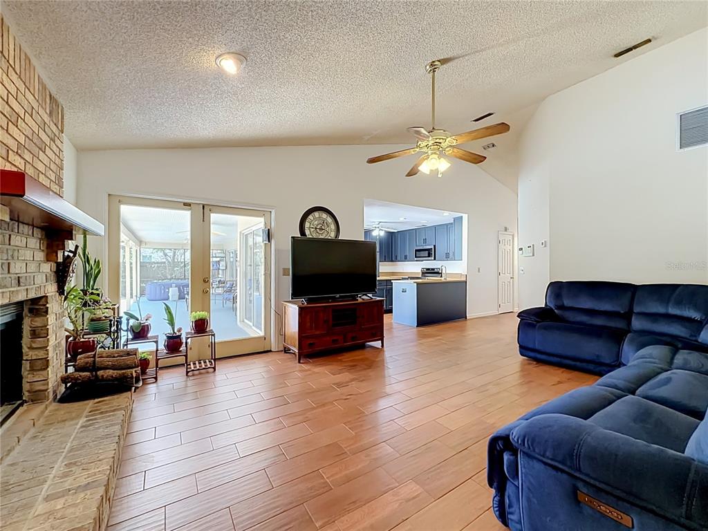 A living room with wood-look tile floors, a brick fireplace, and a view into the kitchen — 5427 SAGO PALM COURT, ORLANDO, FL