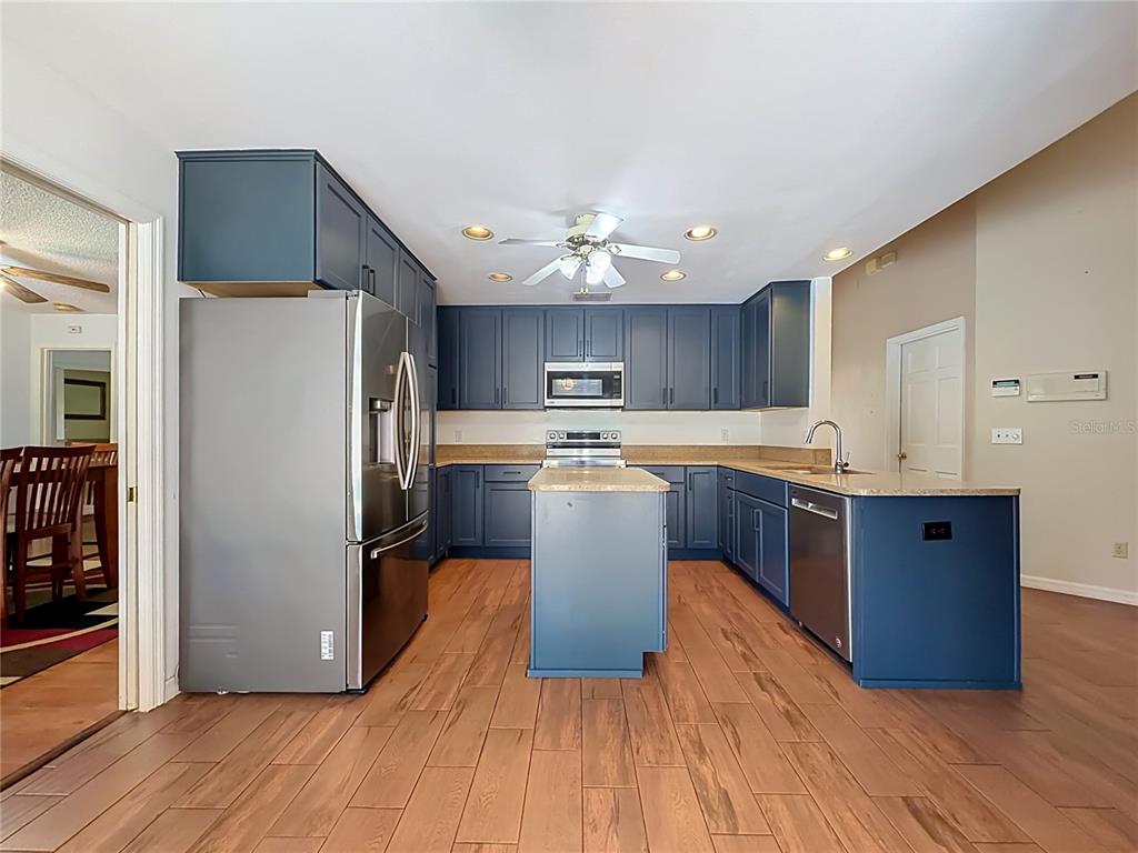 A kitchen features blue cabinets, stainless steel appliances, a central island, and wood-look flooring — 5427 SAGO PALM COURT, ORLANDO, FL