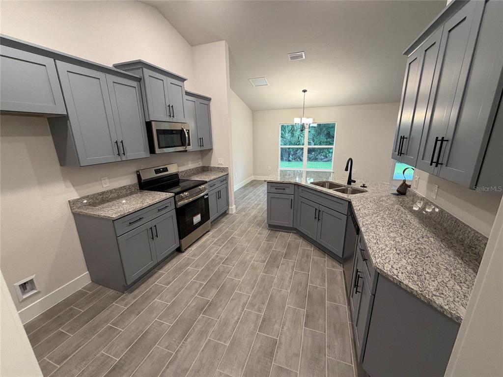A kitchen features gray cabinets, granite countertops, stainless steel appliances, and wood-look tile flooring — 20237 NAVAJO LANE, PORT CHARLOTTE, FL