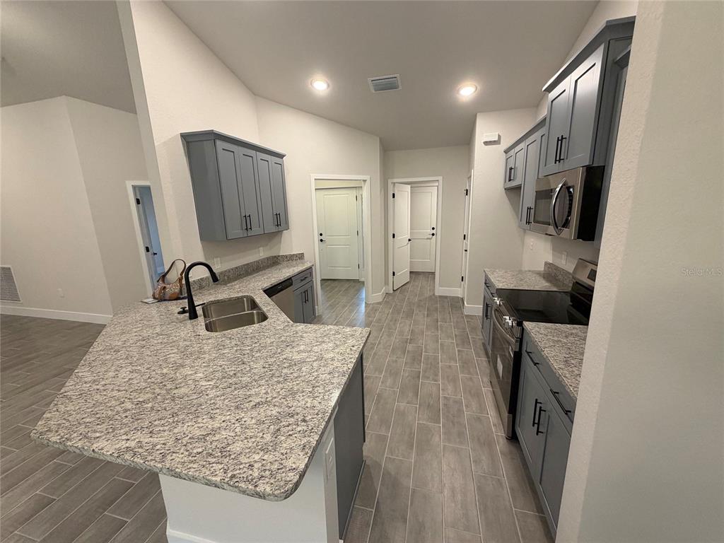 A kitchen features gray cabinets, granite countertops, stainless steel appliances, and gray tile flooring — 20237 NAVAJO LANE, PORT CHARLOTTE, FL