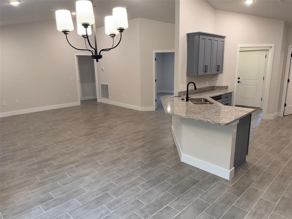 An open-concept kitchen and dining area features gray tile flooring, granite countertops, and a chandelier — 20237 NAVAJO LANE, PORT CHARLOTTE, FL