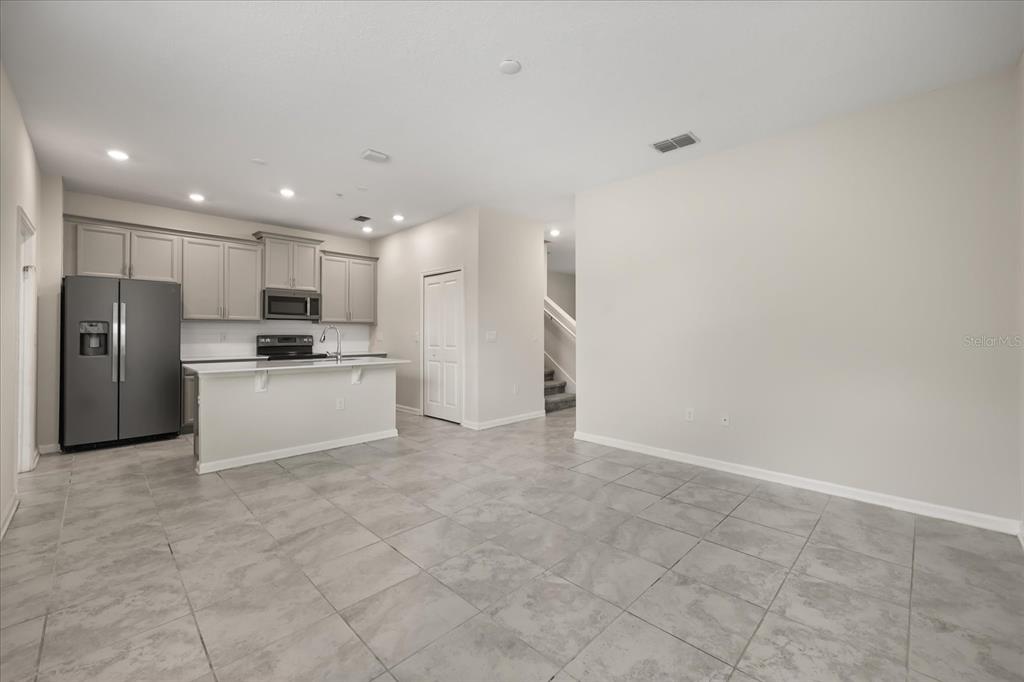An open-concept kitchen features gray cabinets, stainless steel appliances, and light-colored tile flooring — 2966 AQUA VIRGO LOOP UNIT 16, ORLANDO, FL