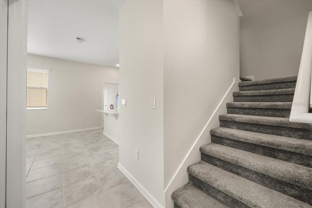 A view of a carpeted staircase next to a tiled room with a kitchen counter — 2966 AQUA VIRGO LOOP UNIT 16, ORLANDO, FL