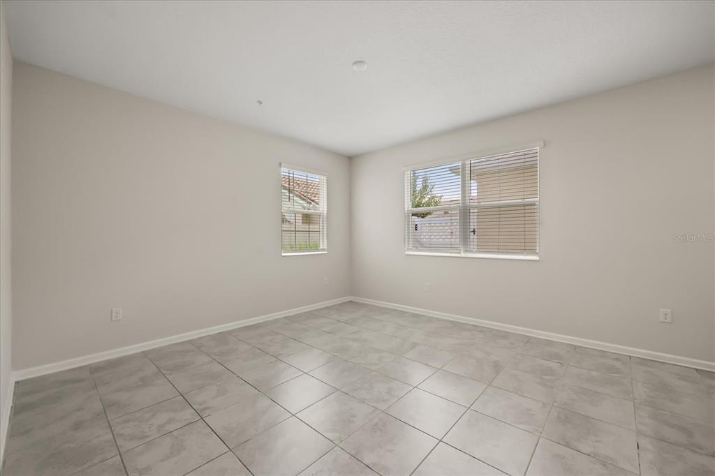 An empty room features light gray tile flooring, neutral walls, and two windows with blinds — 2966 AQUA VIRGO LOOP UNIT 16, ORLANDO, FL