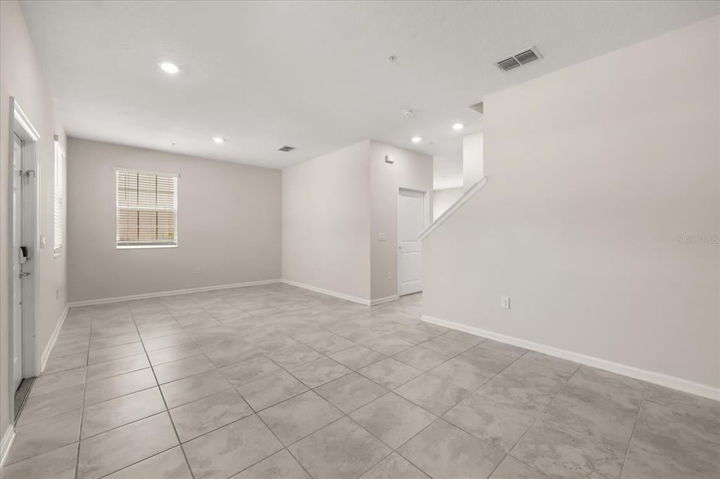 An empty room features light gray tile flooring, white walls, and a staircase — 2966 AQUA VIRGO LOOP UNIT 16, ORLANDO, FL