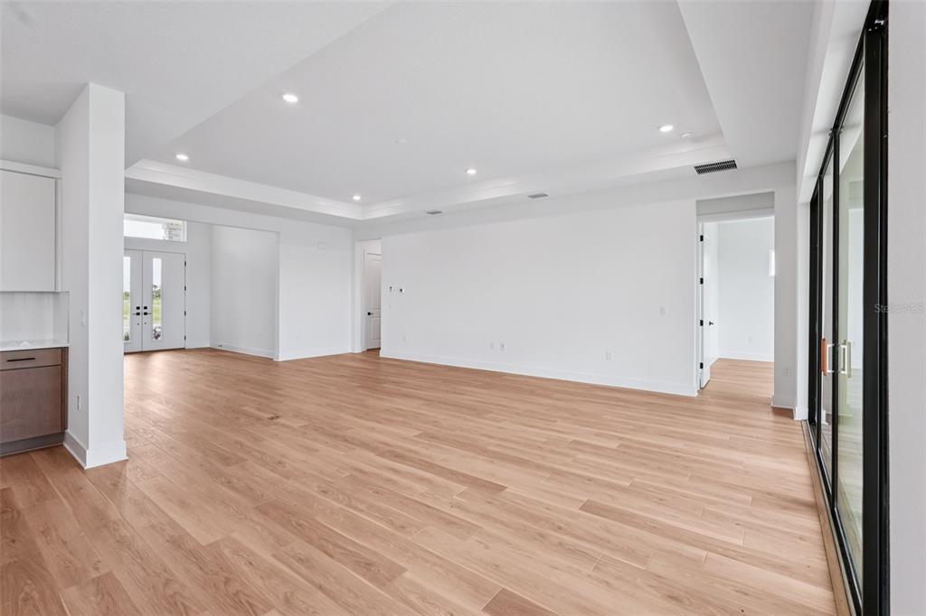 An open-concept living area features light wood flooring, white walls, and a tray ceiling — 8320 GOLDEN BEACH COURT, PARRISH, FL