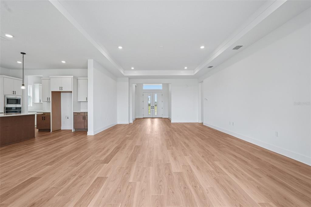 An open-concept living area features light wood flooring, white walls, and a tray ceiling — 8320 GOLDEN BEACH COURT, PARRISH, FL
