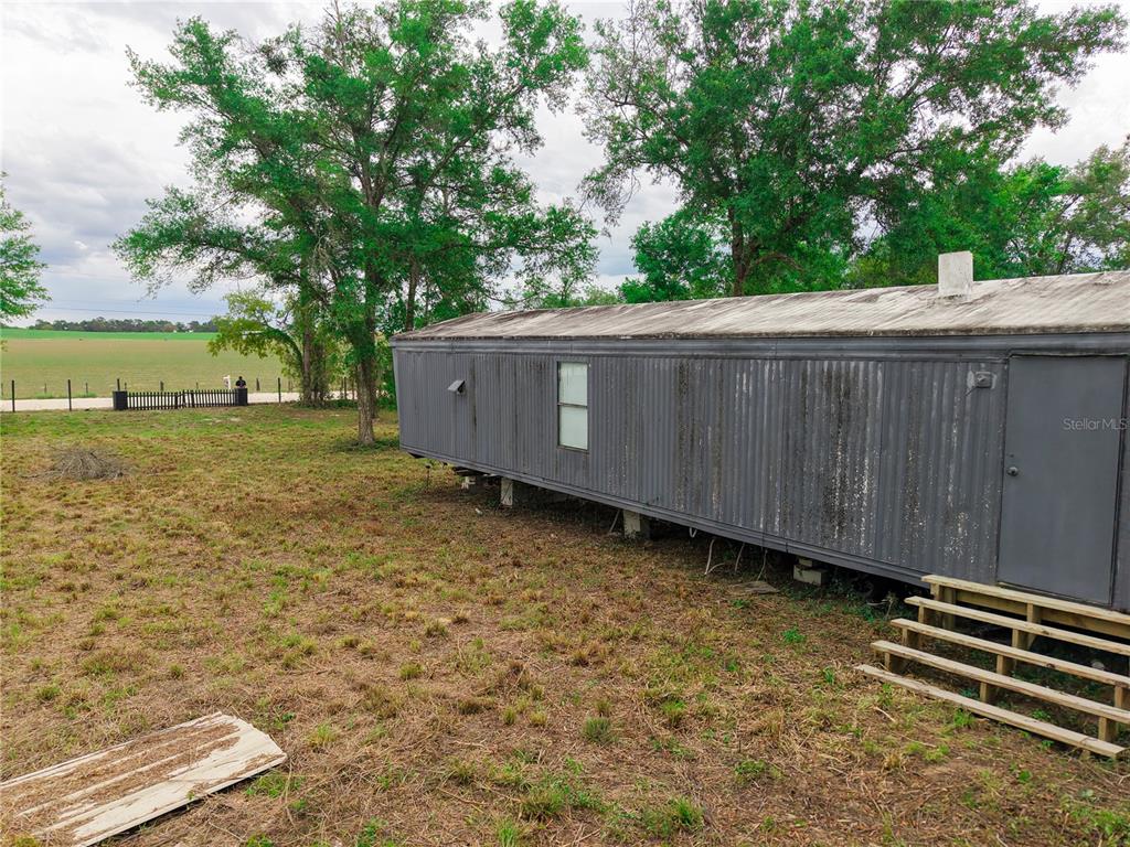 A gray mobile home sits on a grassy lot next to a large open field — 1390 NE 130TH AVENUE, WILLISTON, FL