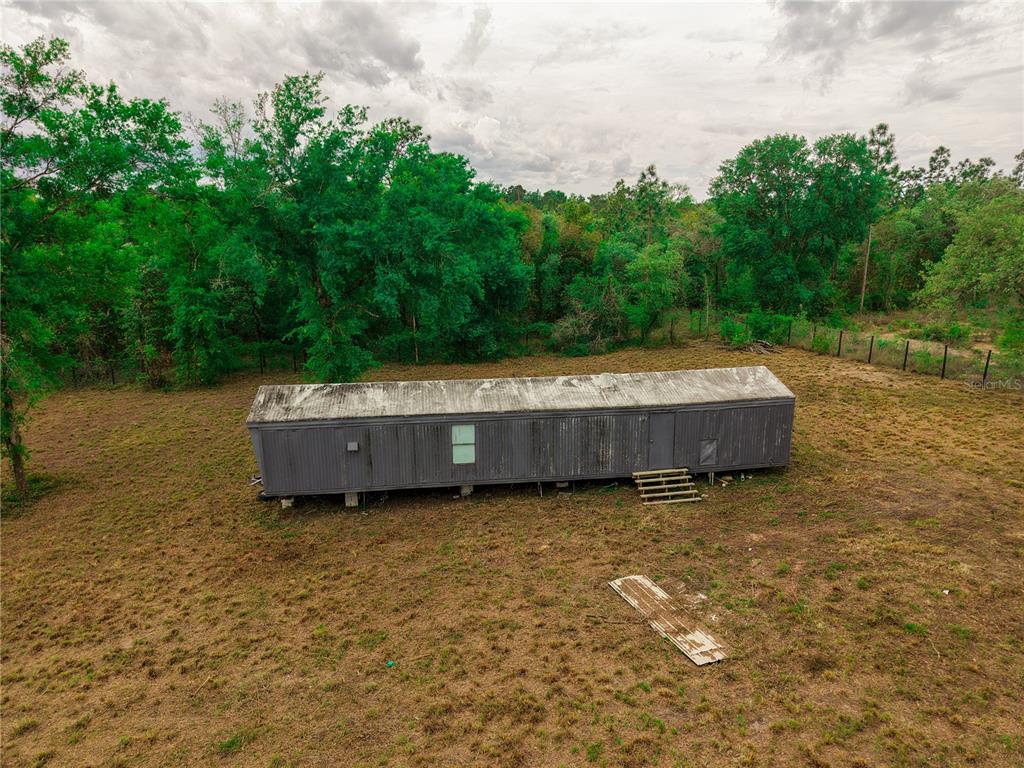 An aerial view shows a long, weathered mobile home situated on a large, grassy lot — 1390 NE 130TH AVENUE, WILLISTON, FL