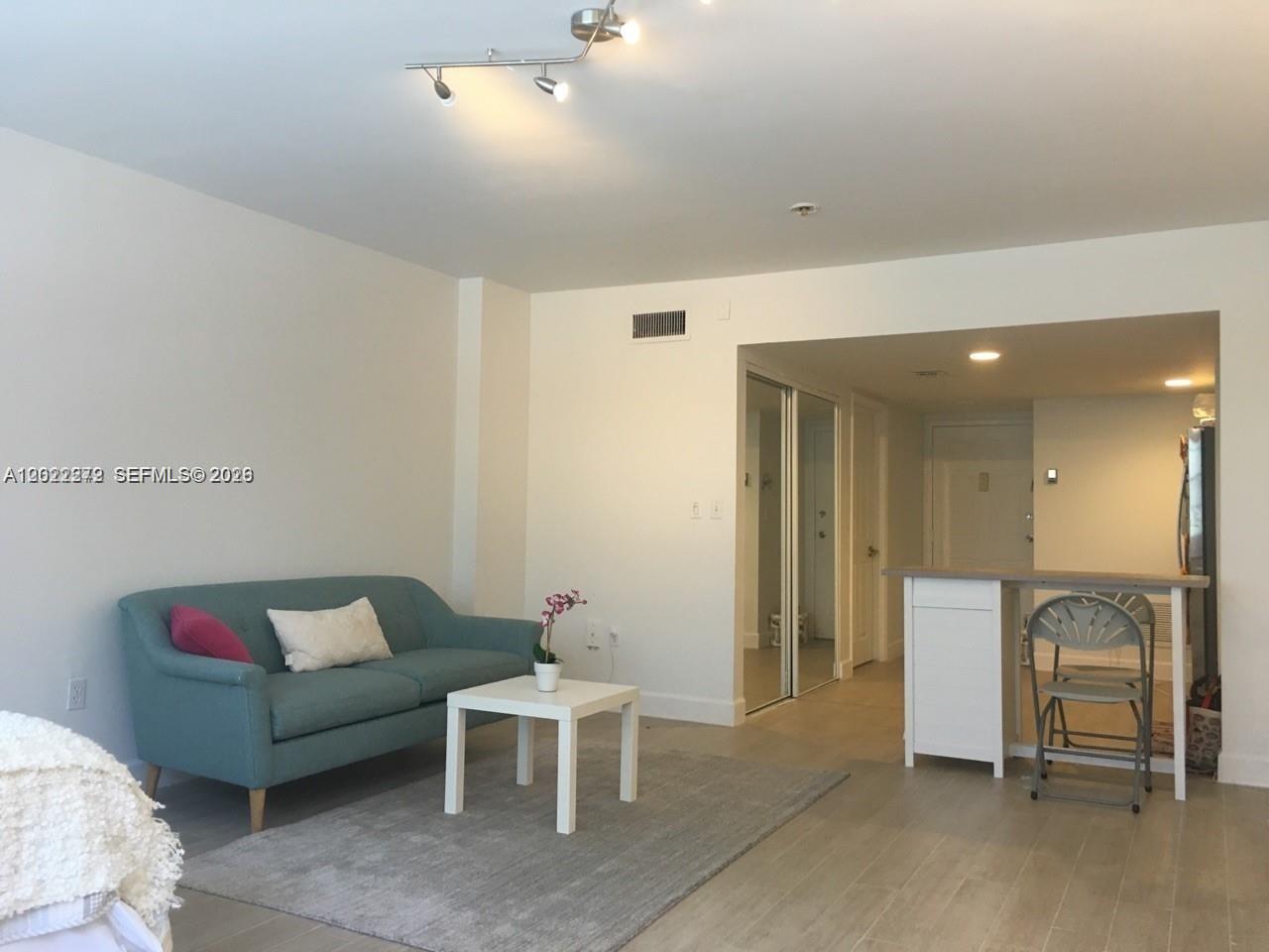 A living room features a blue sofa, white coffee table, and an adjacent kitchen counter — 999 Brickell Bay Dr # 209, Miami FL 33131, MIAMI, FL