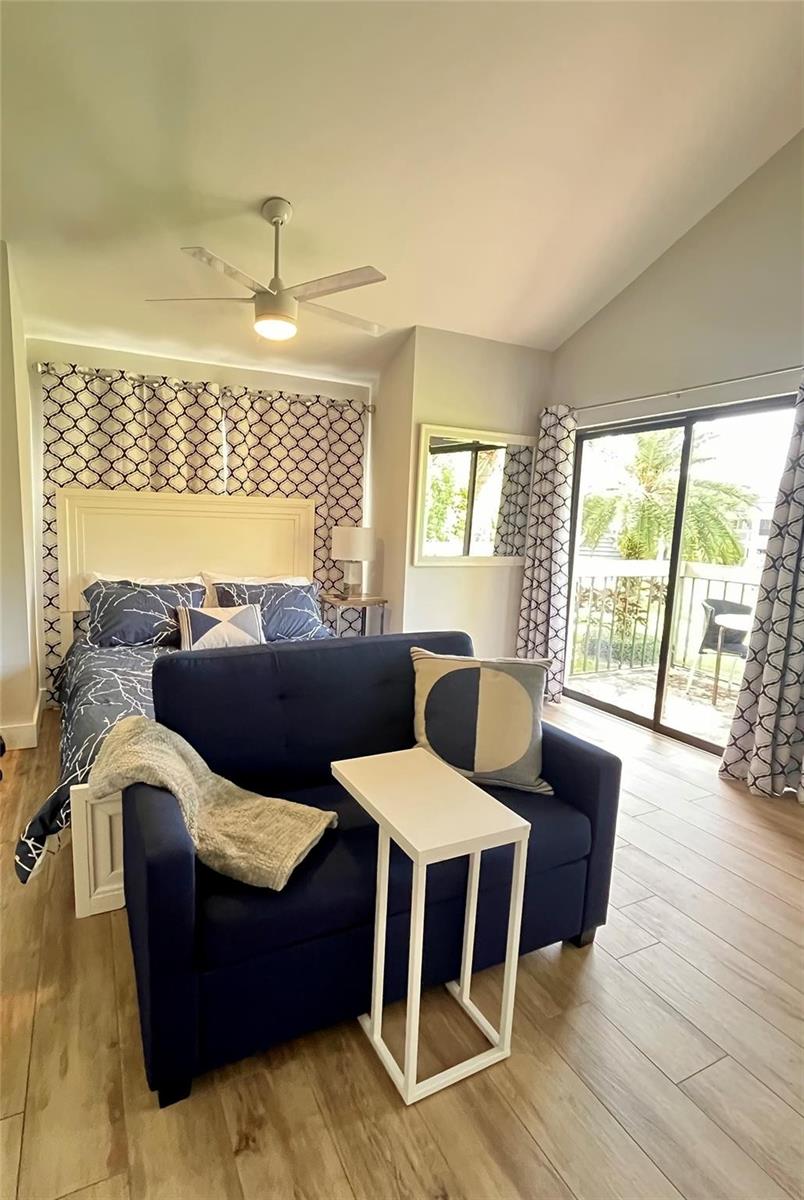 A bedroom features a blue sofa, a bed with patterned bedding, and a sliding glass door — 11863 Wimbledon Circle # 536, Wellington FL 33414, WELLINGTON, FL