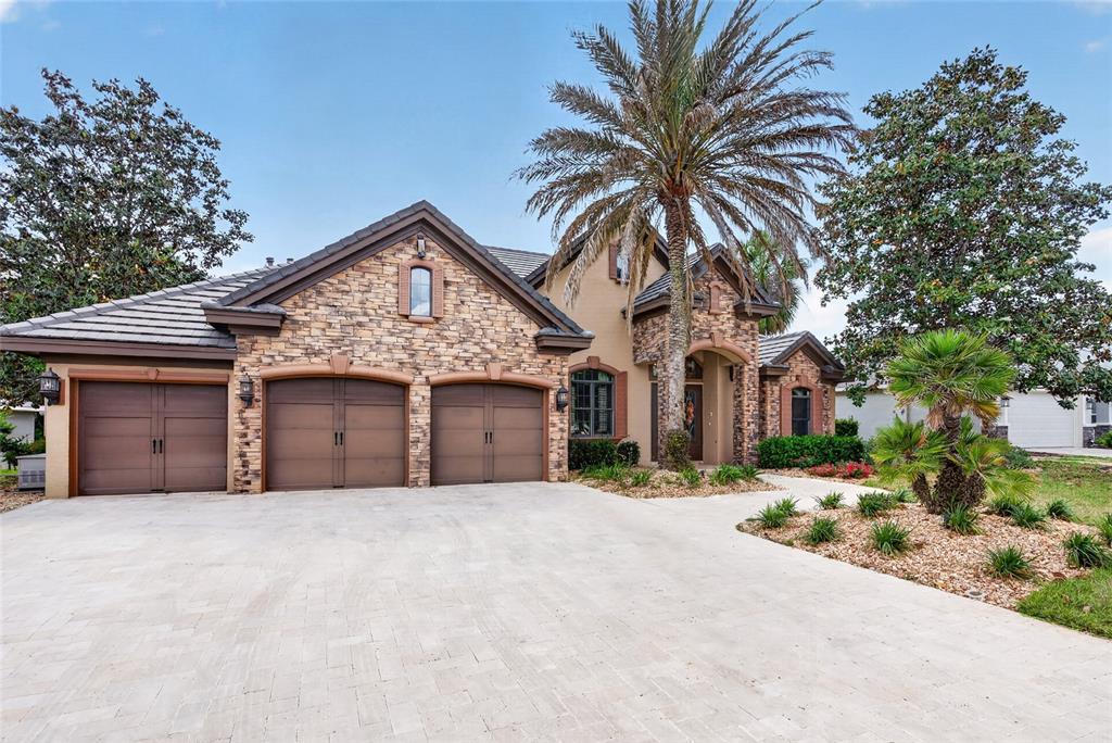 A single-story house with a stone facade, three garage doors, and a tall palm tree — 6662 SW 179TH AVENUE ROAD, DUNNELLON, FL