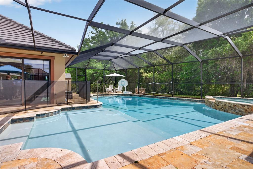 A screened-in swimming pool with a spa and stone patio sits behind a residential home — 6662 SW 179TH AVENUE ROAD, DUNNELLON, FL