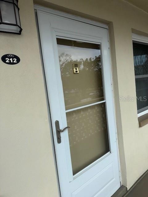 A white storm door with a glass panel and a brass handle on a beige exterior — 1051 79TH AVENUE N UNIT 212, ST PETERSBURG, FL