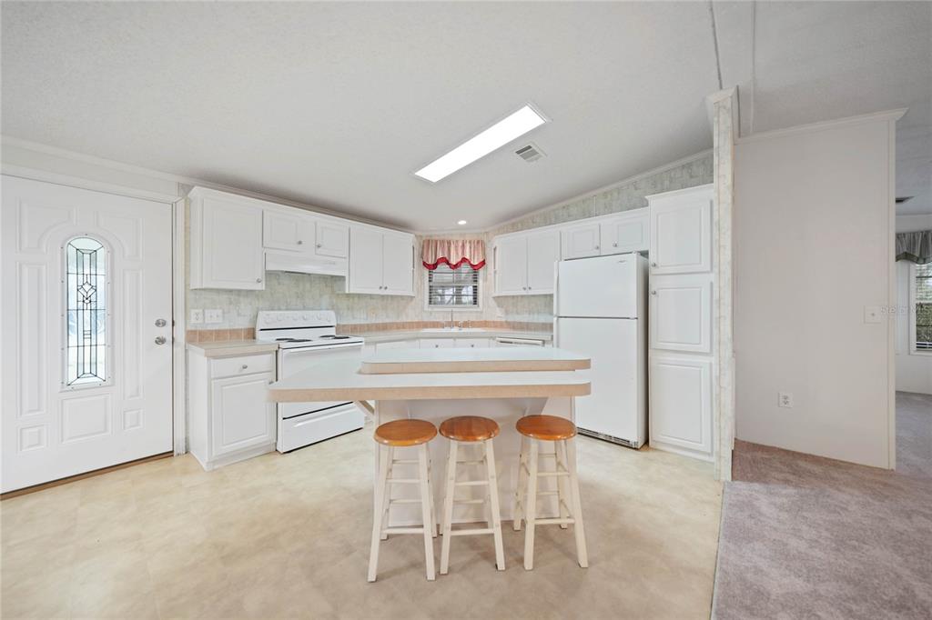 A kitchen features white cabinets, a central island with three stools, and white appliances — 2100 KINGS HIGHWAY UNIT 517, PORT CHARLOTTE, FL