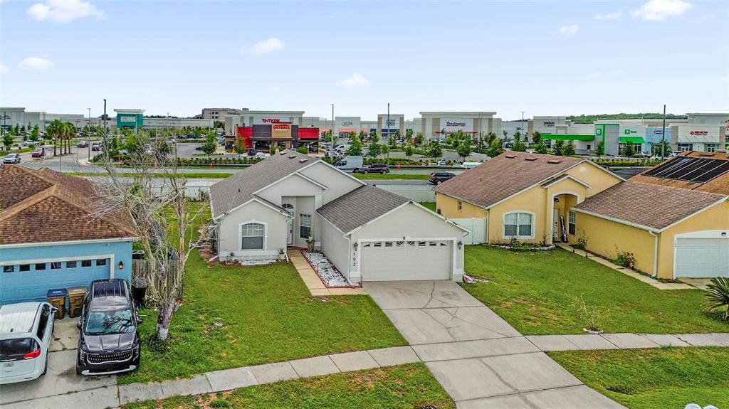 An aerial view shows a suburban house with a driveway and a shopping center nearby — 102 SAFFRON WAY, KISSIMMEE, FL