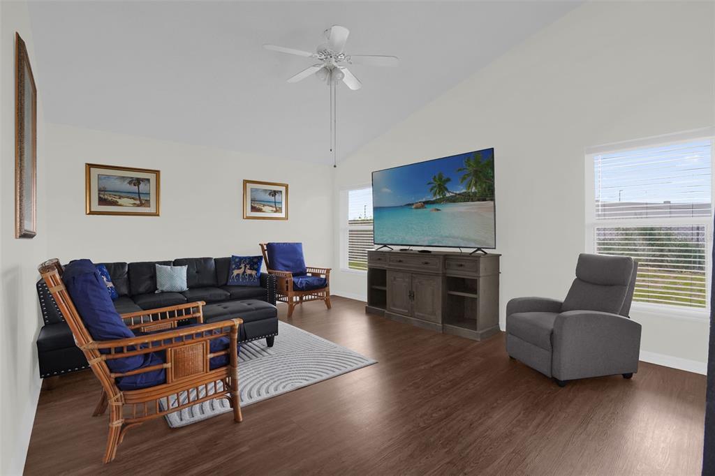 A living room with a black sectional, two rattan chairs, a television, and wood flooring — 102 SAFFRON WAY, KISSIMMEE, FL