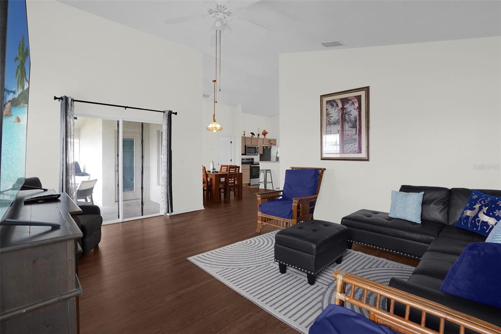 A living room with dark wood floors, a black sectional sofa, and a dining area — 102 SAFFRON WAY, KISSIMMEE, FL