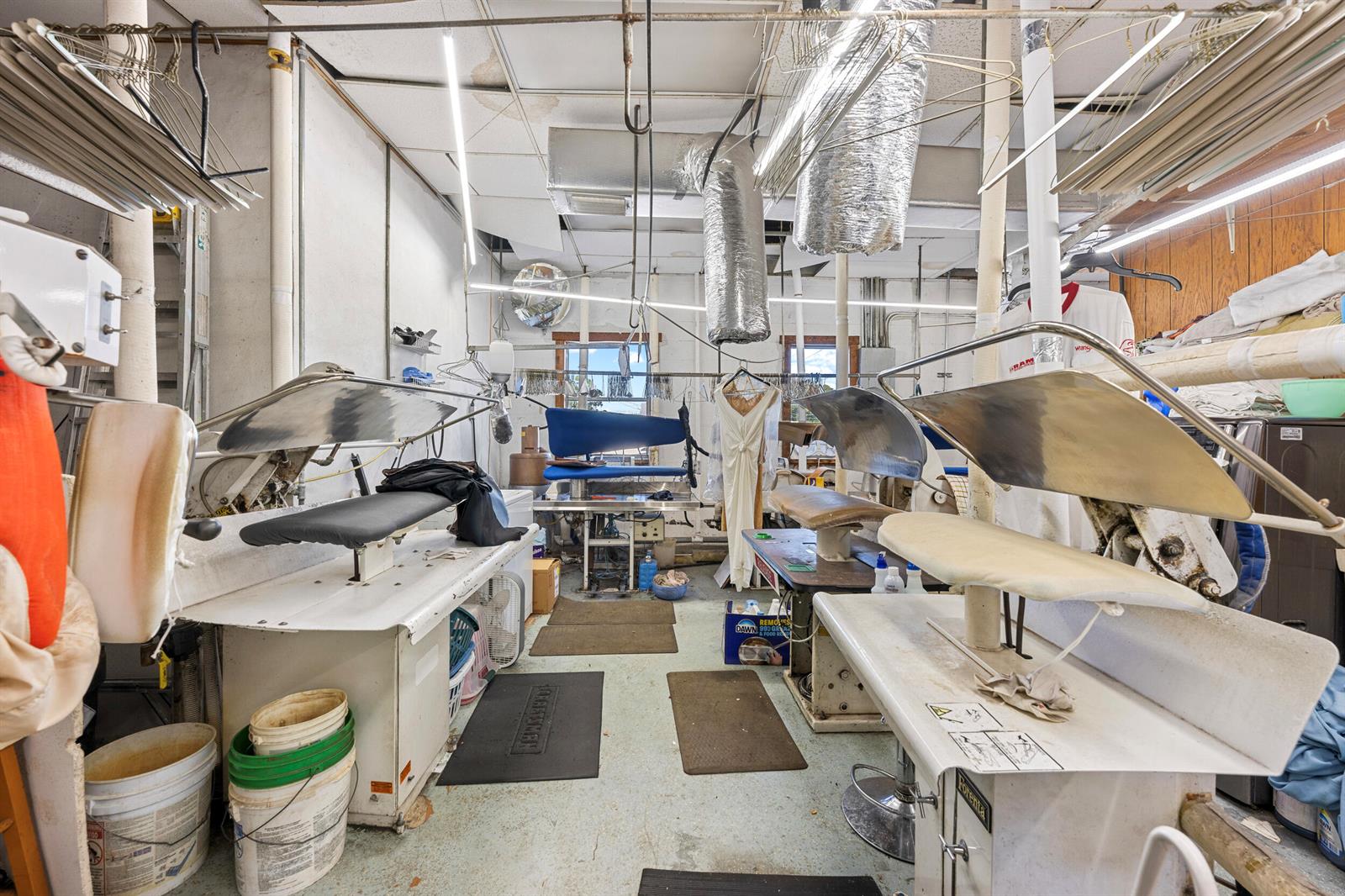 A dry cleaning facility features industrial pressing machines, hanging garment racks, and exposed ceiling ductwork — 400 S Parrott Avenue, Okeechobee FL 34974, OKEECHOBEE, FL