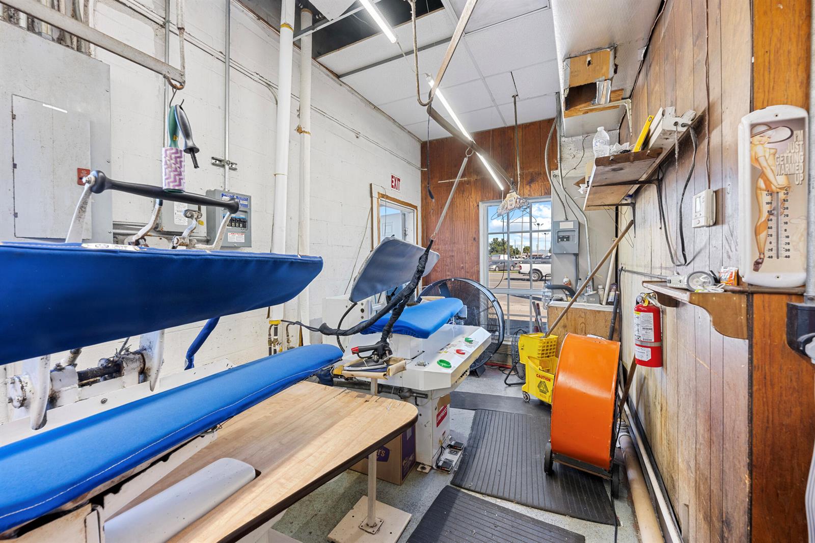A commercial laundry room features industrial pressing equipment, wood-paneled walls, and a large window — 400 S Parrott Avenue, Okeechobee FL 34974, OKEECHOBEE, FL