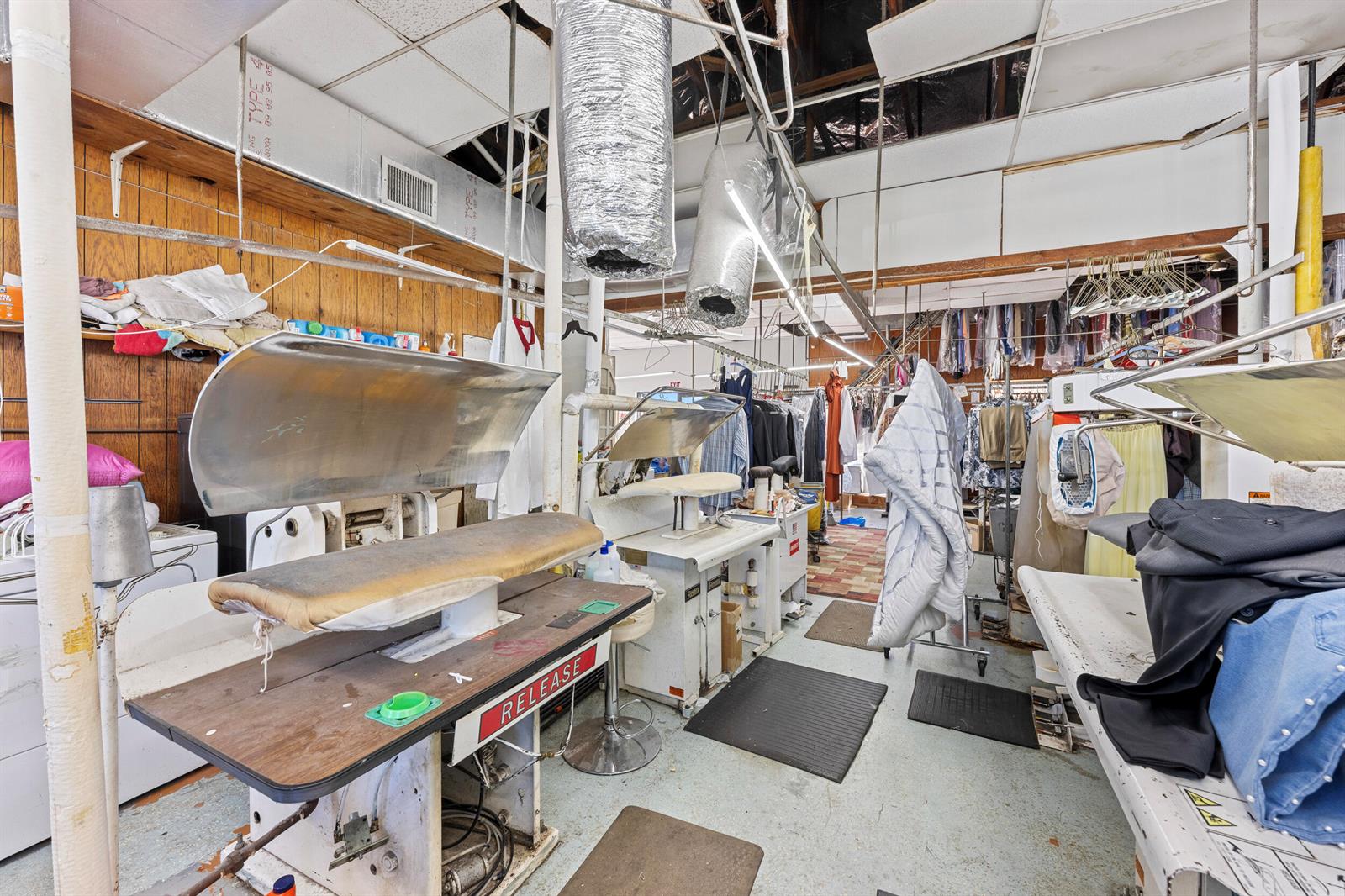 An industrial dry cleaning facility features multiple pressing machines, hanging garments, and exposed ceiling ductwork — 400 S Parrott Avenue, Okeechobee FL 34974, OKEECHOBEE, FL